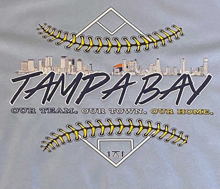 Light blue shirt featuring tampa and stpete skyline with a artists baseball diamond representing the tampa bay rays locally made shirt